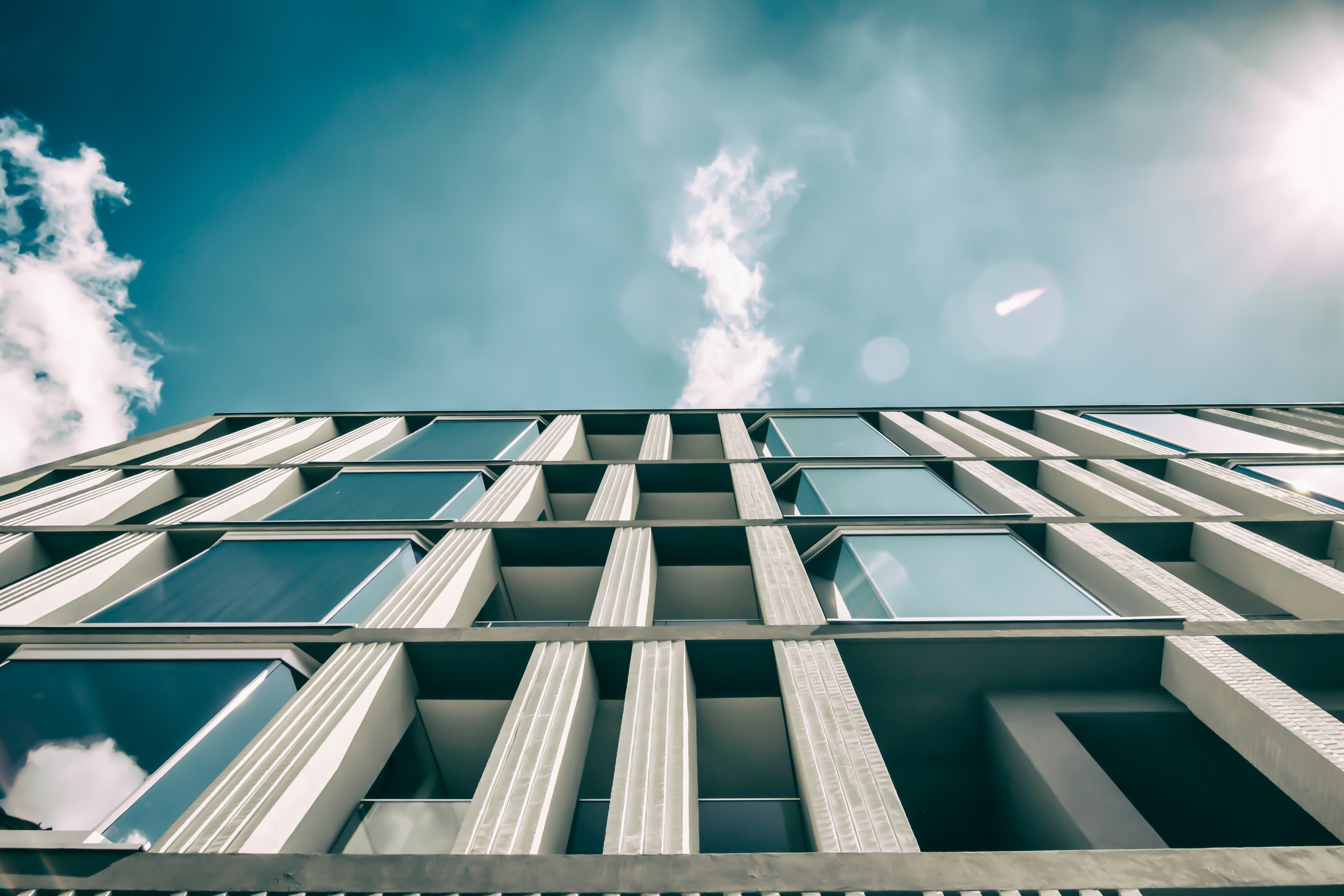 Low-angle view of a modern glass-and-concrete office building facade against a blue sky