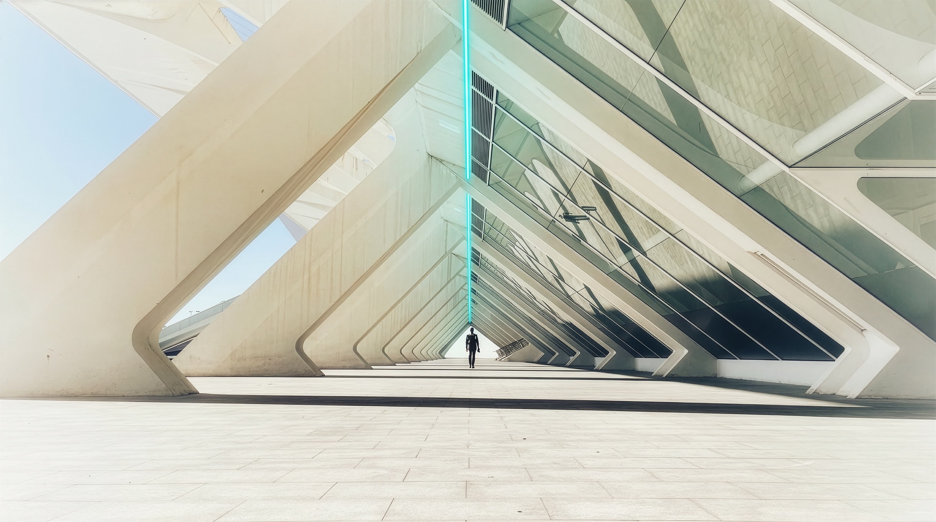 A lone figure walking through a vast, light-filled modern architectural structure